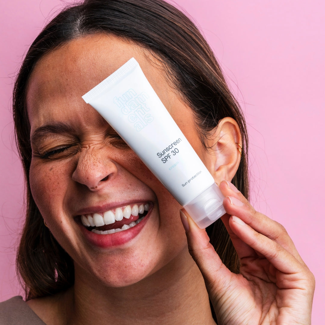 Woman applying sunscreen cream to her face against a pink background